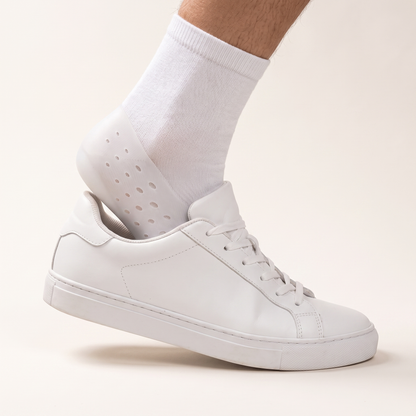 A socked foot wearing the ELVO heel lift stepping into a plain white trainer